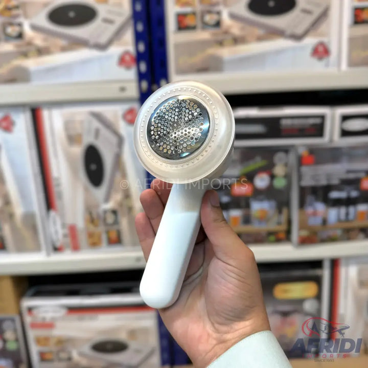 White handheld fabric shaver with a circular metal mesh head.