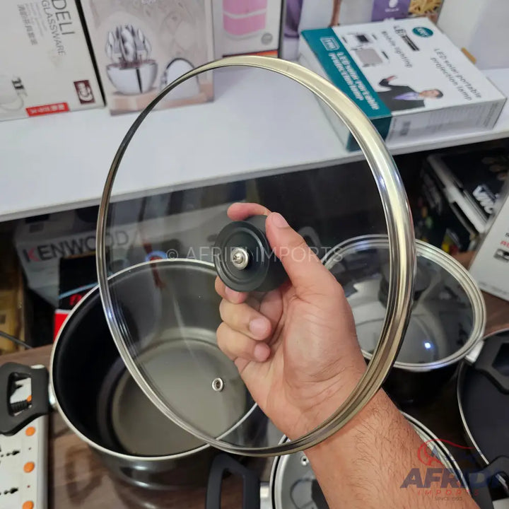 A hand holding a clear glass pot lid with a black knob.