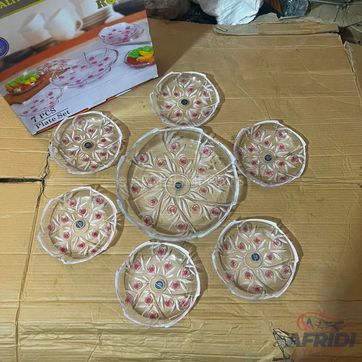 A set of seven clear glass plates with a decorative pattern, including one large serving plate and six smaller individual plates.