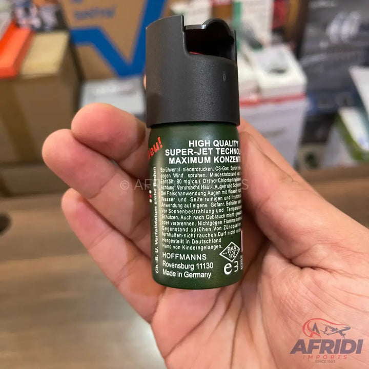 A dark green self-defense spray canister held in a hand.