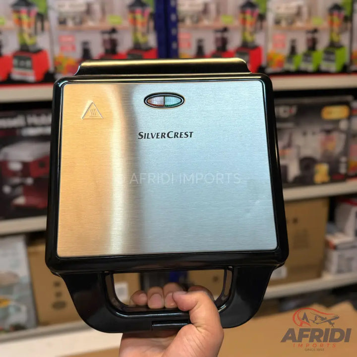 A silver and black sandwich maker held in a hand.