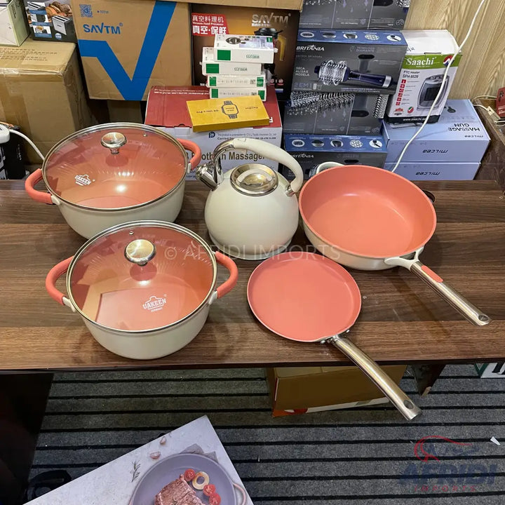 A set of matching peach and white cookware, including two lidded pots, a skillet, a crepe pan, and a tea kettle.