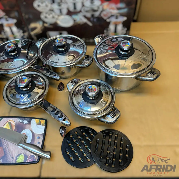 A set of shiny stainless steel pots and pans with clear lids and black handles, accompanied by a kitchen knife and two black trivets.