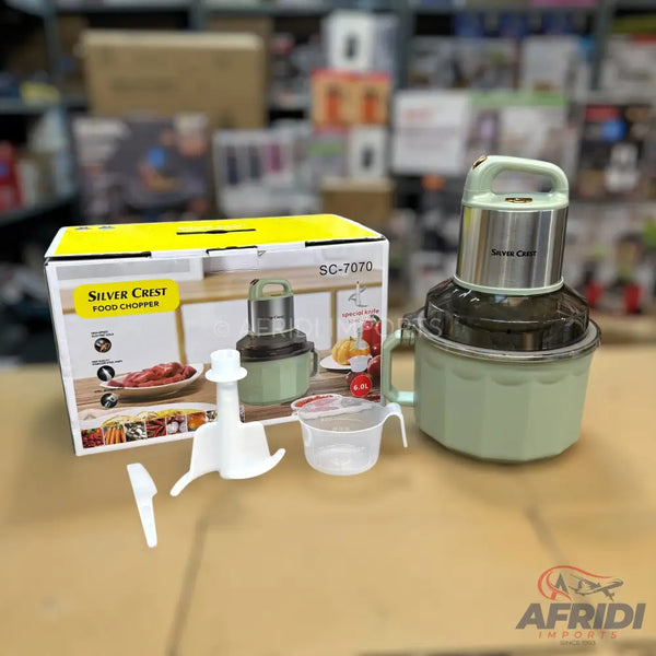 A light green and silver food chopper with a box, accessories, and a measuring cup.