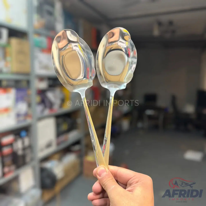 Two shiny, elongated metal spoons held by a hand.