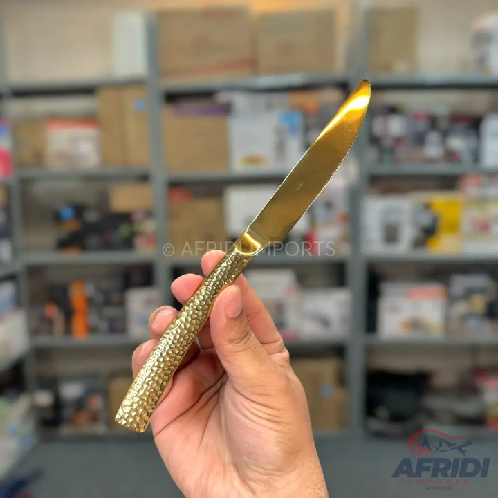A gold-colored dinner knife with a textured, hammered handle.