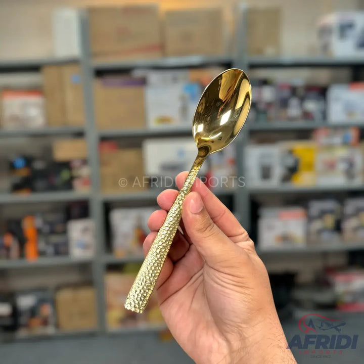 A golden-colored metal spoon with a textured, hammered handle.
