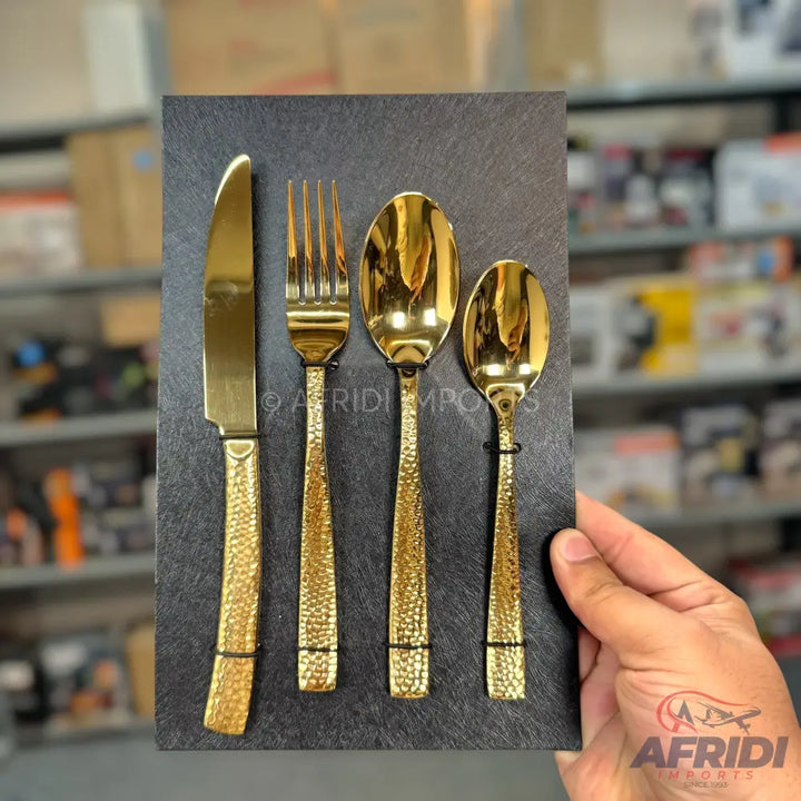 A set of four golden, hammered-texture flatware pieces: a knife, a fork, a large spoon, and a small spoon.