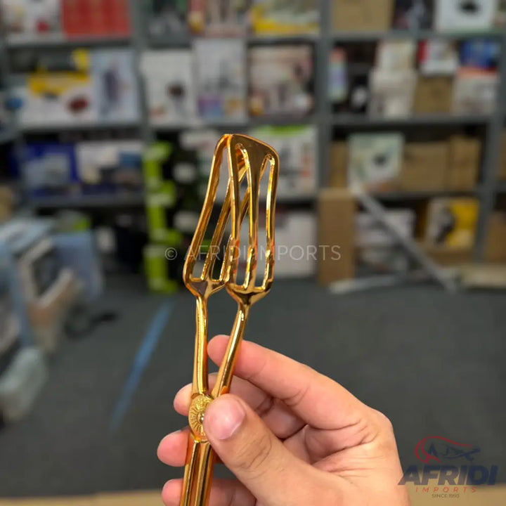 Gold-colored metal serving tongs with fork-like ends.