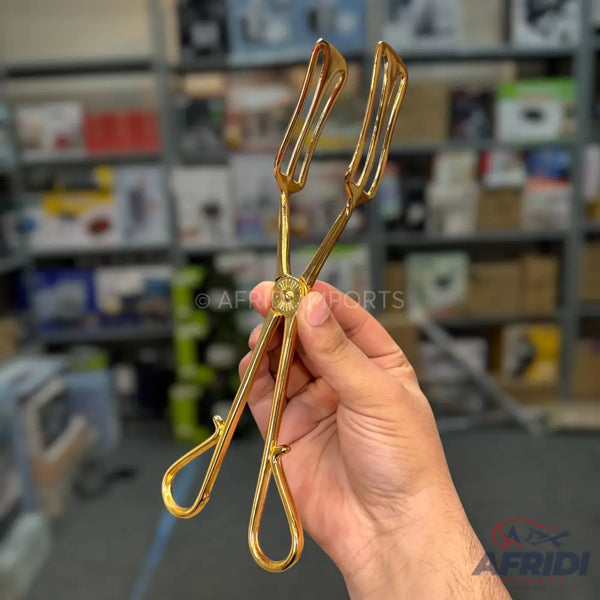 A hand holding golden metal tongs with a decorative pivot point.