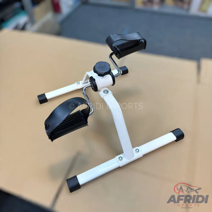 A white and black portable pedal exerciser with adjustable resistance.
