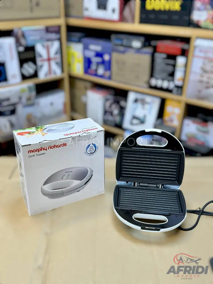 A white and black opened electric sandwich maker with ridged plates, next to its retail box.