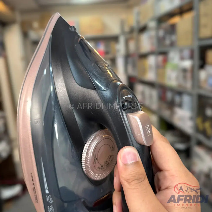 A dark grey and rose gold steam iron with a textured temperature dial and a power button.