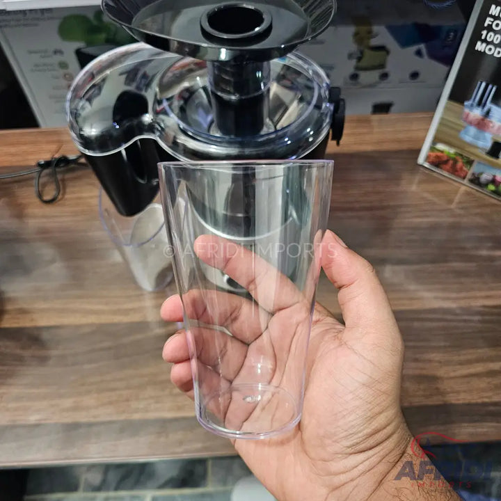 A clear plastic drinking cup held in a hand, with a juicer in the background.