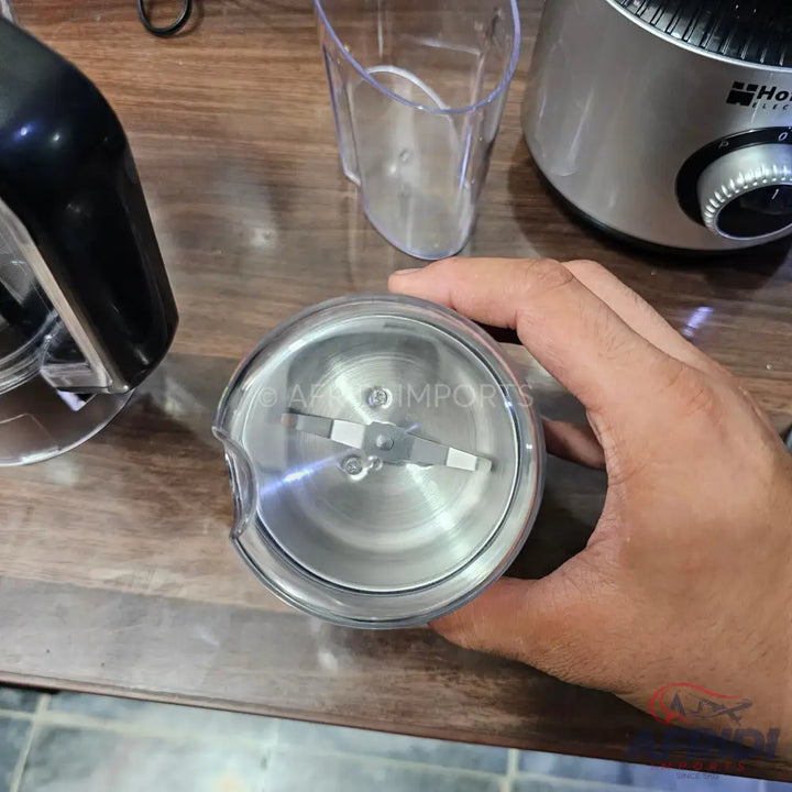 A clear plastic blender cup with a stainless steel blade assembly.