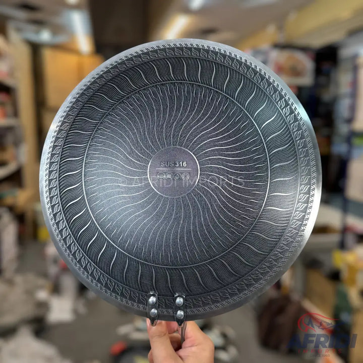 The underside of a round, dark-colored pan with a textured, sunburst-like pattern and a raised rim design.