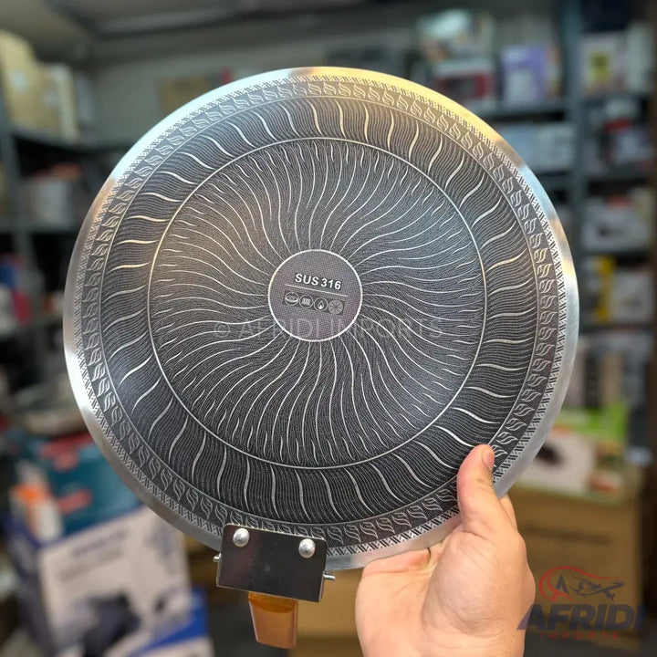 The underside of a stainless steel cooking pan with a decorative, heat-distributing pattern.