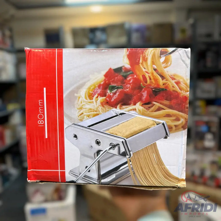A pasta maker with a fresh sheet of dough being cut into noodles, displayed on a box featuring a plate of spaghetti with tomato sauce.