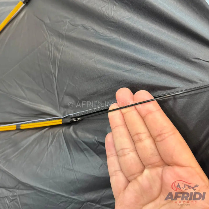 A person’s hand holding a thin black elastic cord in front of a dark, wrinkled fabric.