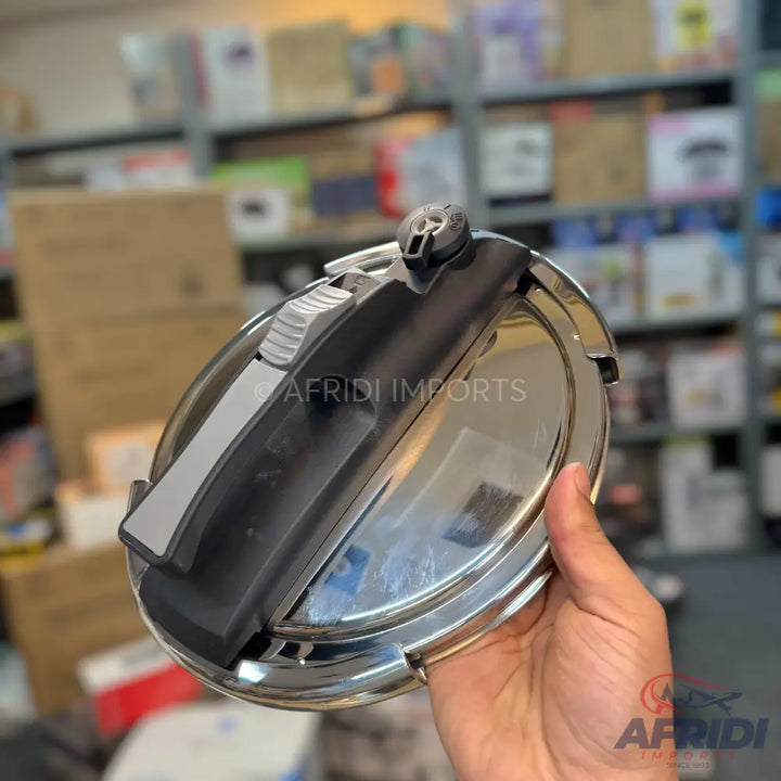A shiny, metallic pressure cooker lid with a black and gray handle mechanism.