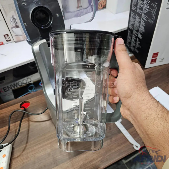A transparent plastic blender pitcher with a black handle and a removable blade assembly.