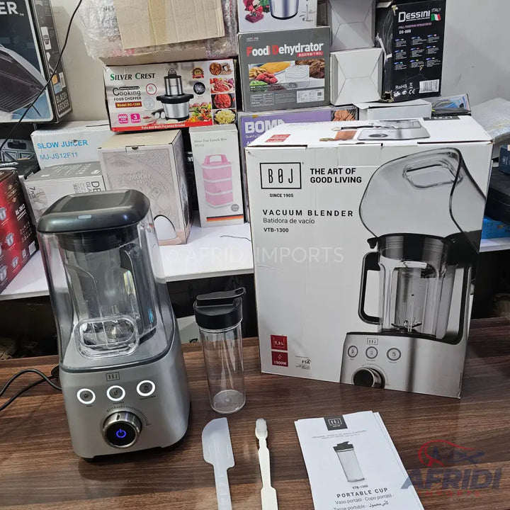 A silver vacuum blender with a clear pitcher, a portable cup, and cleaning tools.