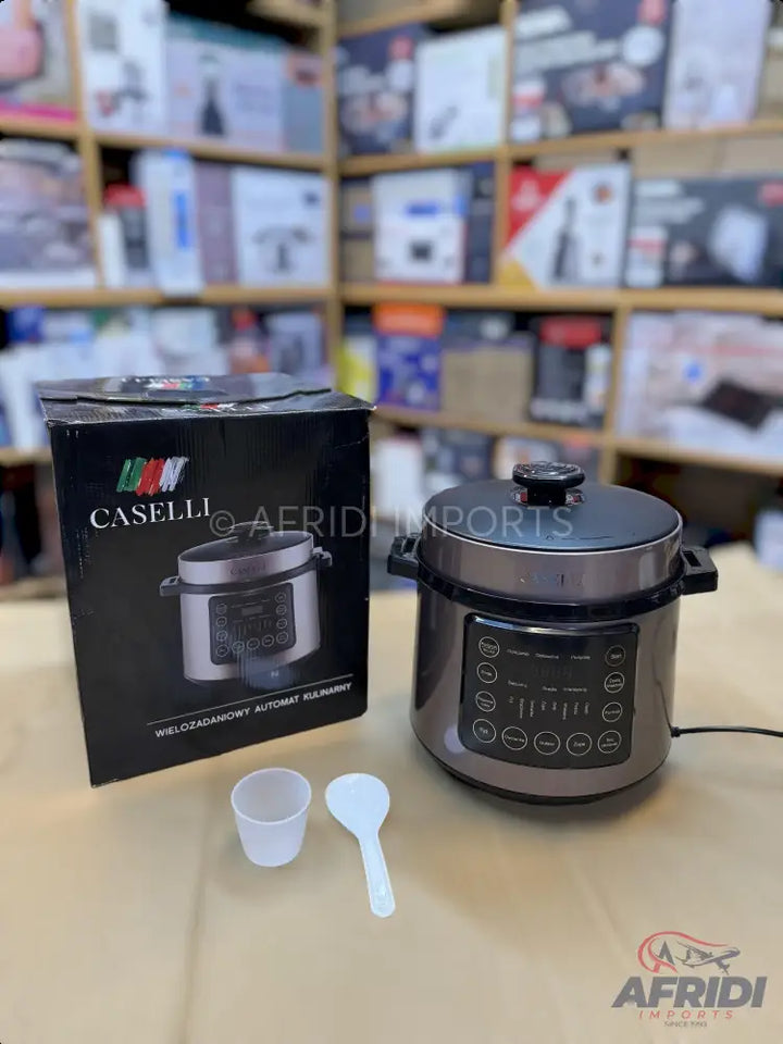 A dark grey electric pressure cooker with a digital control panel, accompanied by its box, a measuring cup, and a serving spoon.