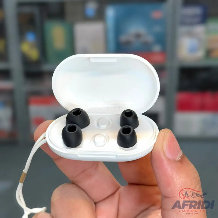 A white, open charging case for earbuds, containing four black silicone ear tips.