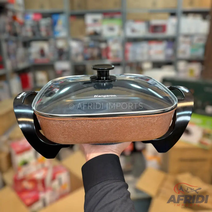 A rectangular electric cooking pot with a glass lid and two handles, featuring a textured brown body.