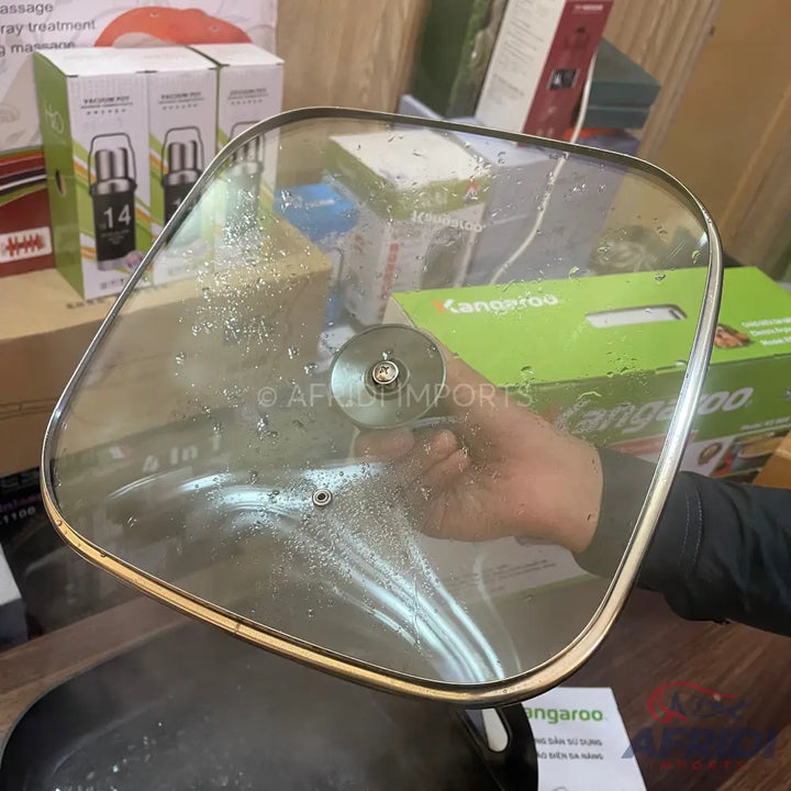 A square glass lid with a gold-colored rim and a central silver knob, showing condensation from steam.