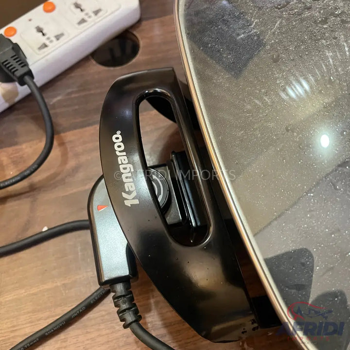 A black electric cooking pot with a handle, power cord, and temperature control.