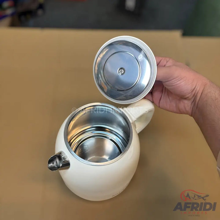 An off-white electric kettle with a stainless steel interior and an open lid being held.