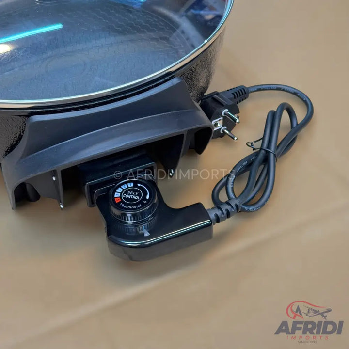 Black electric skillet with a glass lid and a detachable temperature control probe.
