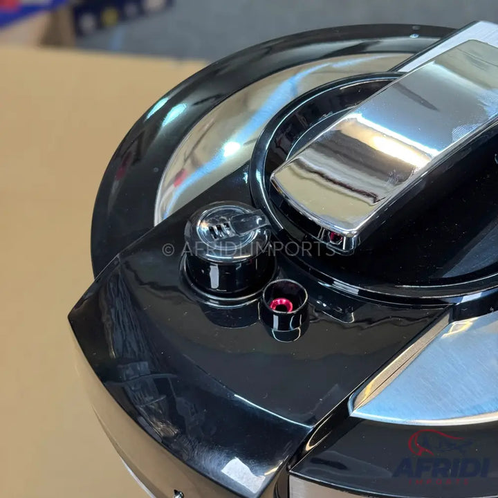A glossy black pressure cooker lid with chrome accents and a steam release valve.