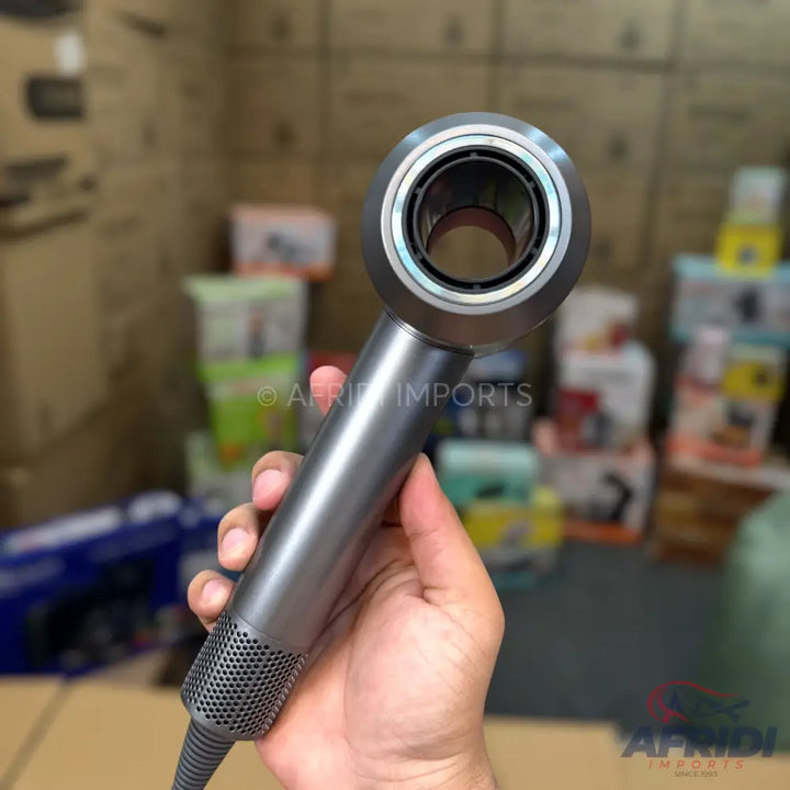 A person holding a grey, handheld, cylindrical hair dryer with a circular, hollow nozzle.