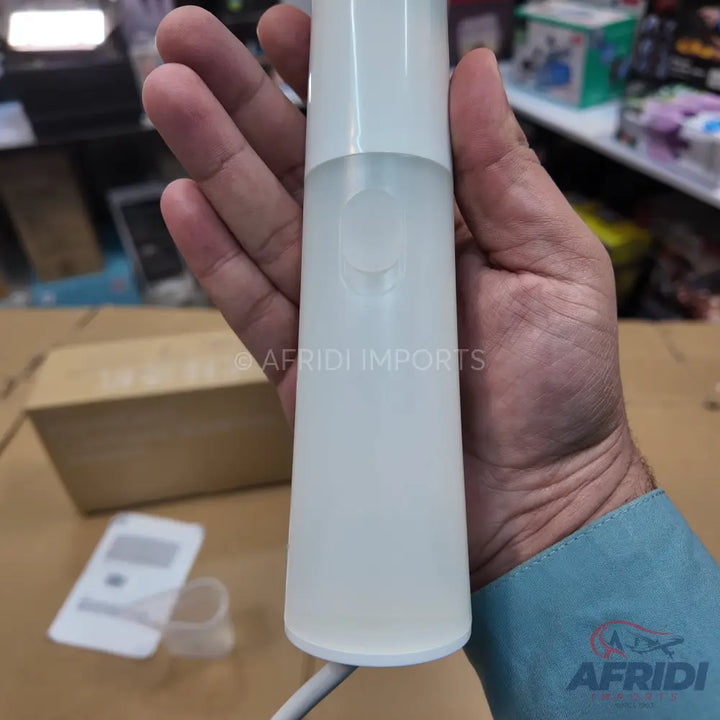 A white, translucent, cylindrical bottle with a white cap, likely containing a liquid, possibly a mist sprayer or diffuser, held in a hand.
