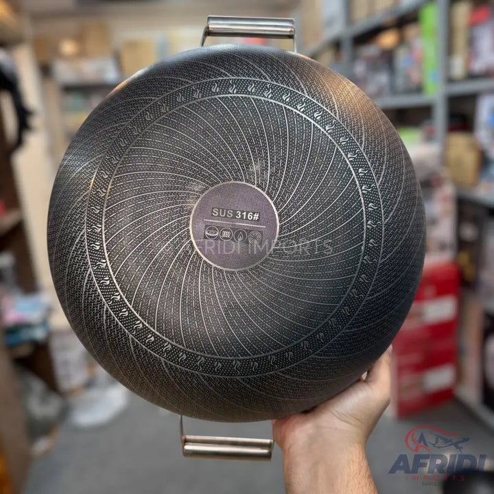 Bottom of a dark-colored wok or deep pan with a textured, concentric pattern and a central circular induction-compatible base.