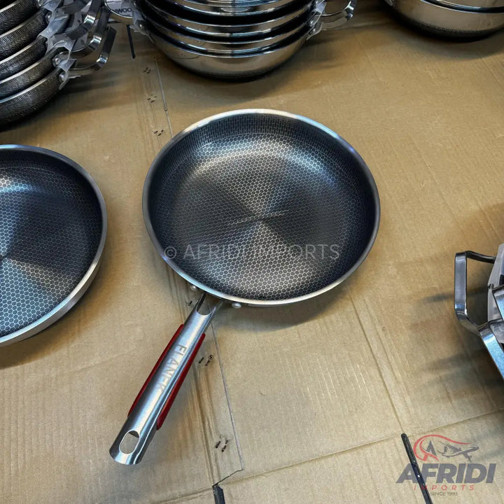 Stainless steel frying pan with a honeycomb pattern and red handle accent.