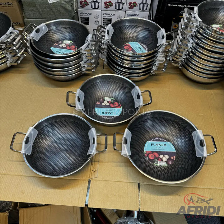 Stacks of black non-stick woks with silver handles.