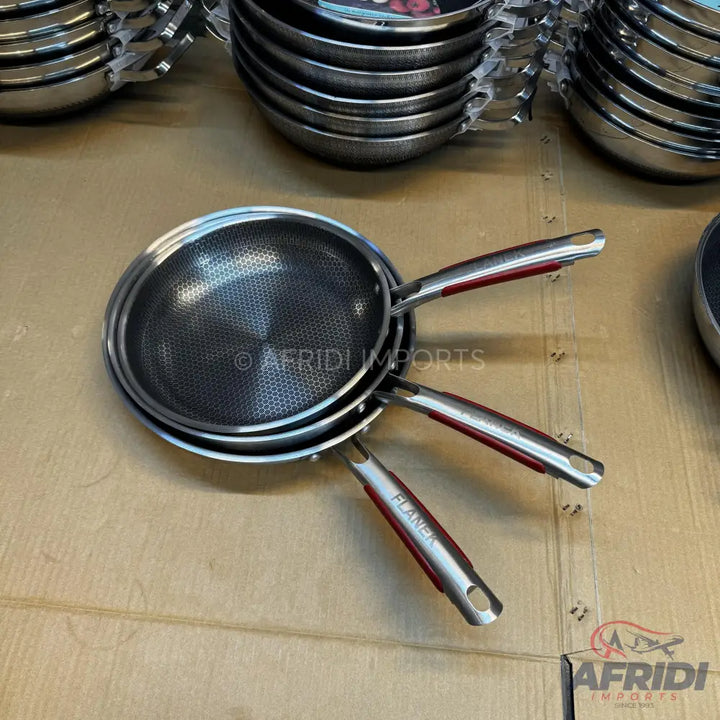 A stack of three stainless steel frying pans with textured non-stick surfaces and red-accented handles.