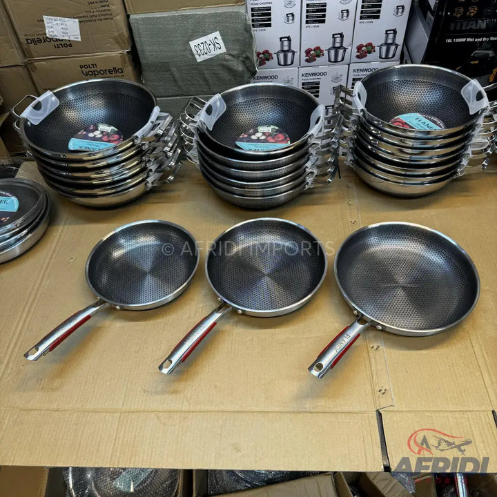Various sizes of stainless steel woks and frying pans with textured non-stick surfaces and red-accented handles.