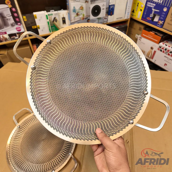 A round, double-handled metal sieve or strainer with a finely perforated, honeycomb-patterned base and a decorative wavy border.
