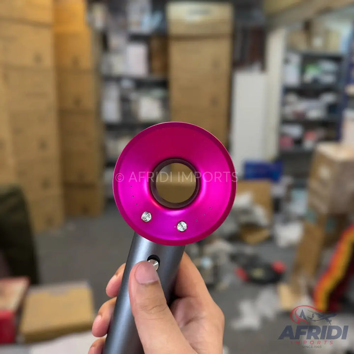 A person holding a pink and gray Dyson Supersonic hair dryer.