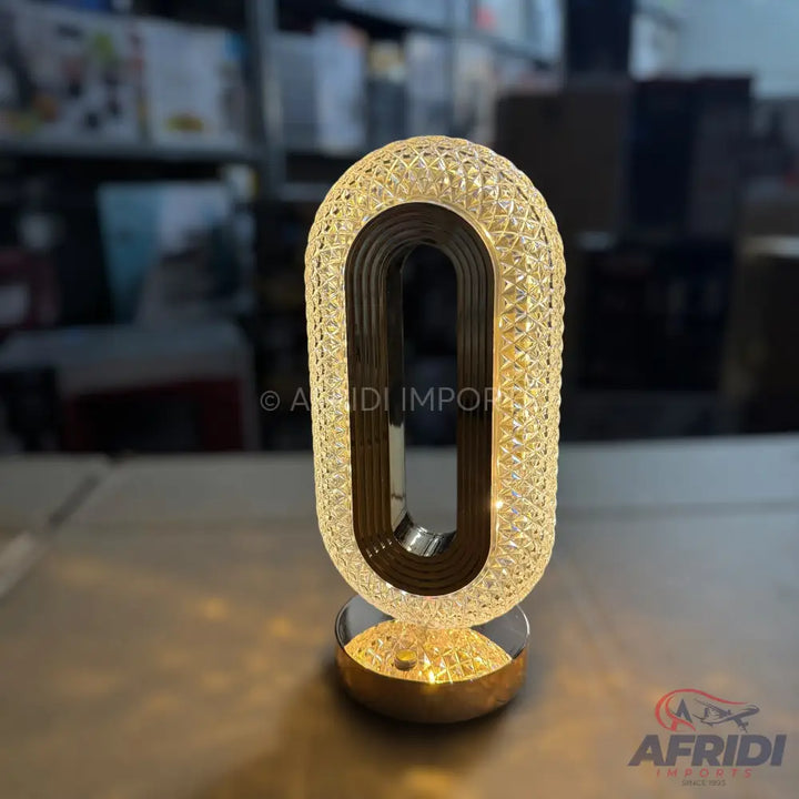 An illuminated, U-shaped table lamp with a crystal-patterned exterior and a metallic base.