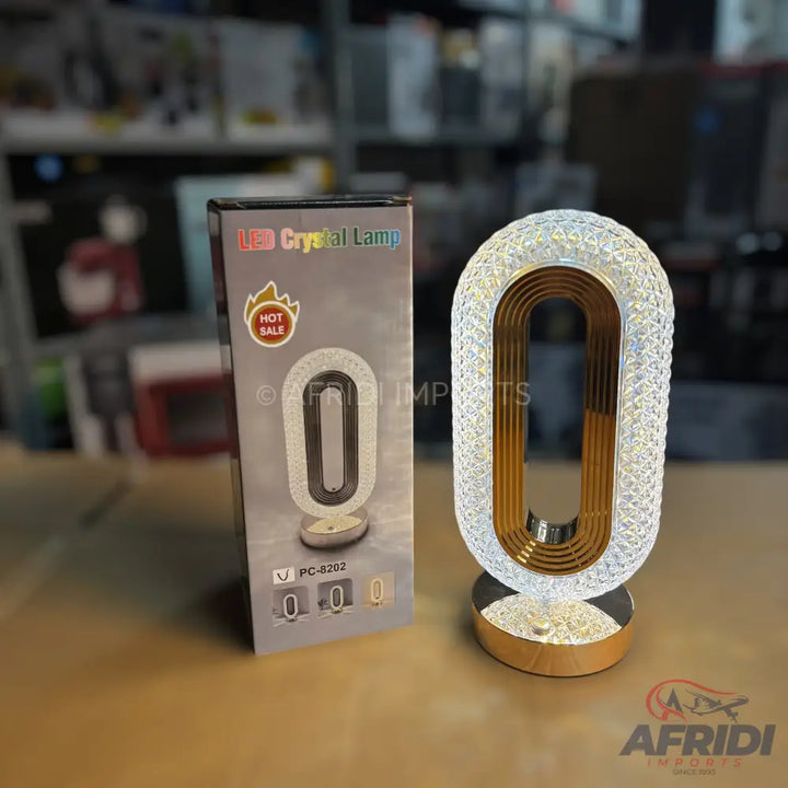 An LED crystal table lamp with a gold-colored base and an oval, hollow design.
