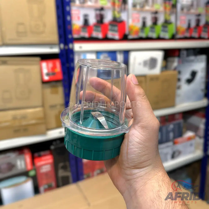 A clear plastic blender cup with a green base and a single blade.