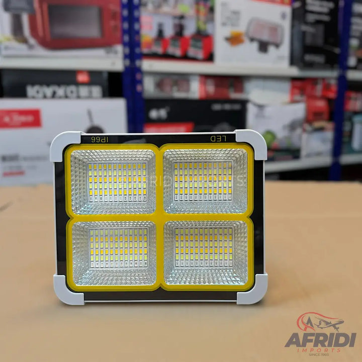 A bright, square-shaped LED floodlight with four distinct light panels, featuring a yellow interior border and a white exterior frame.