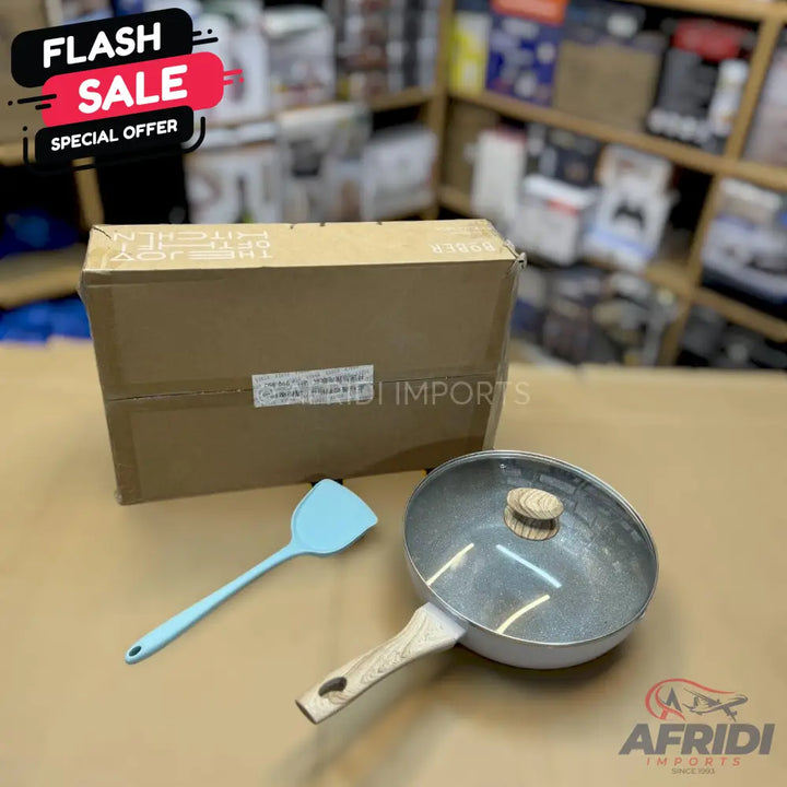 A non-stick frying pan with a glass lid and a light blue spatula.
