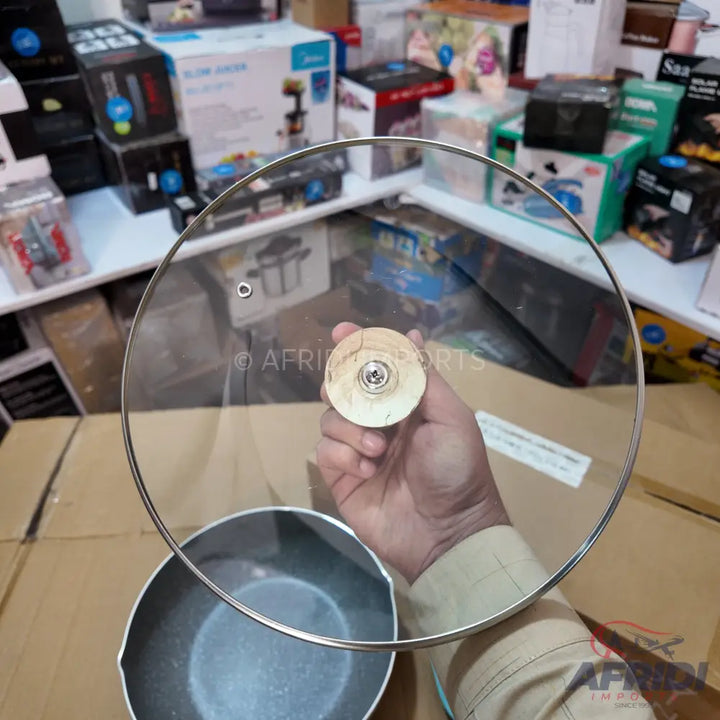 A transparent glass pot lid with a wooden handle.