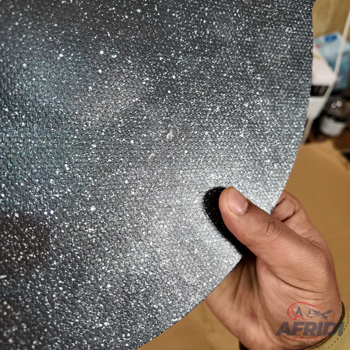 A dark, textured mat or sheet with a speckled, possibly anti-slip surface.